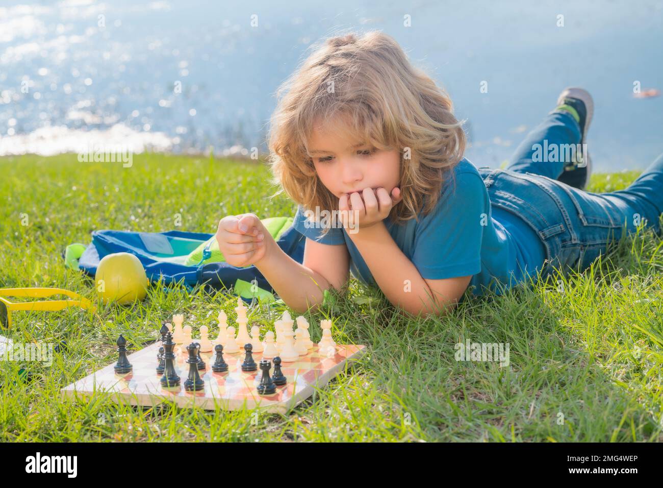 Konzentrierter Junge, der Schachstrategie entwickelt, Brettspiele im Garten spielt, auf Gras liegt. Stockfoto