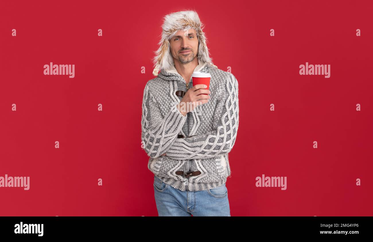 Ein gut aussehender Mann trägt einen Pullover und einen Winterhut, um die Kaffeetasse zu halten Stockfoto