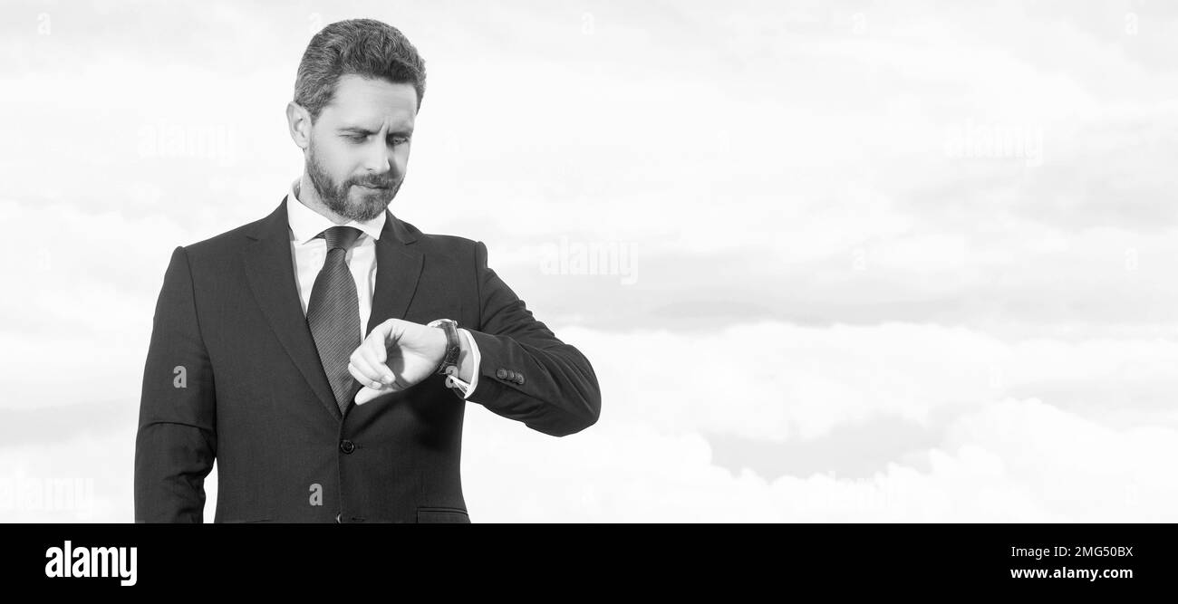 Geschäftsmann in einem Geschäftsanzug, der die Zeit vor dem Hintergrund des Himmels überprüft. Mann Gesicht Porträt, Banner mit Kopieplatz. Stockfoto