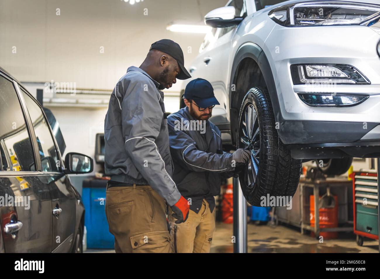 Mittellange Aufnahme von zwei Mechanikern, die ein Autorad reparieren. Werkstattkonzept. Hochwertiges Foto Stockfoto