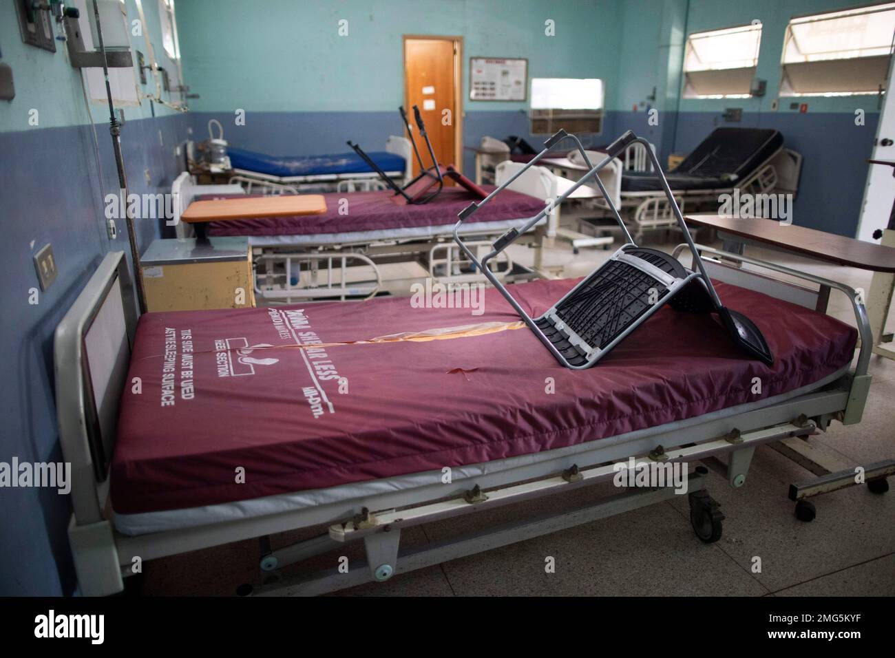 Hospital beds with torn mattresses and chairs stored on them fill a