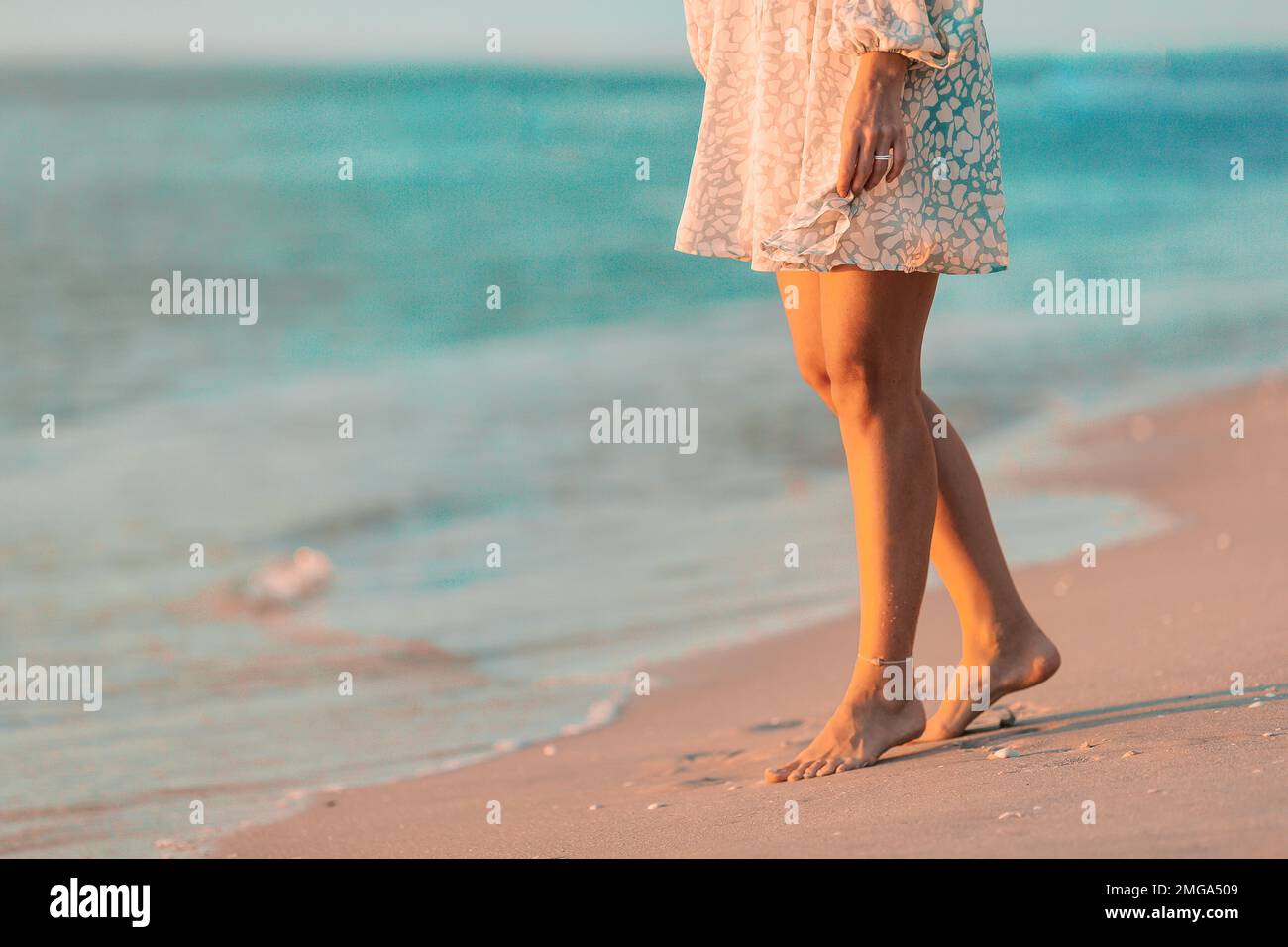 Weibliche Beine in der Nahaufnahme am Strand. Eine Frau in einem Kleid, die am Strand spaziert Stockfoto