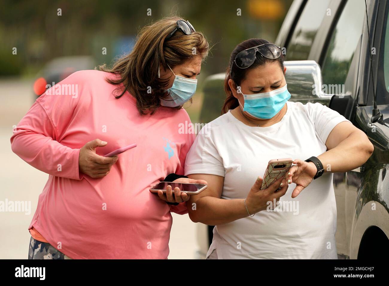 Women wear masks as they check a mobile phone Wednesday, July 1, 2014, in Houston. Harris County Commissioners have voted to extend the recently-issued mask order until August 26. The order directs any businesses providing goods or services to require all employees and visitors to wear face coverings in areas of close proximity to co-workers or the public. (AP Photo/David J. Phillip) Stockfoto