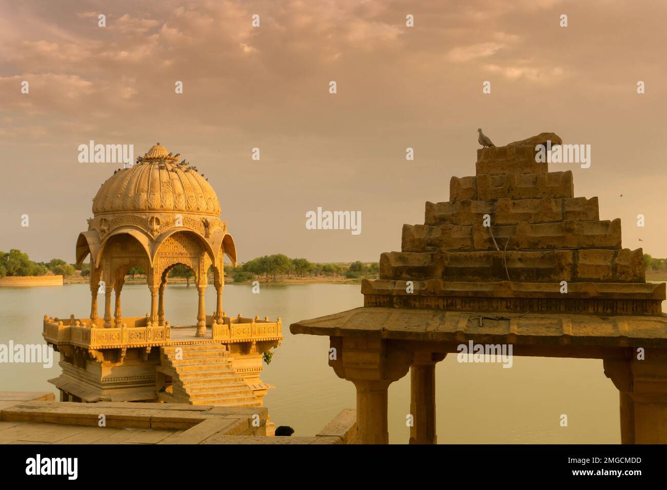 Chhatris und Schreine der hinduistischen Götter und Göttinnen am Gadisar-See, Jaisalmer, Rajasthan, Indien. Indo-islamische Architektur, Sonnenuntergang und bunte Wolken Stockfoto