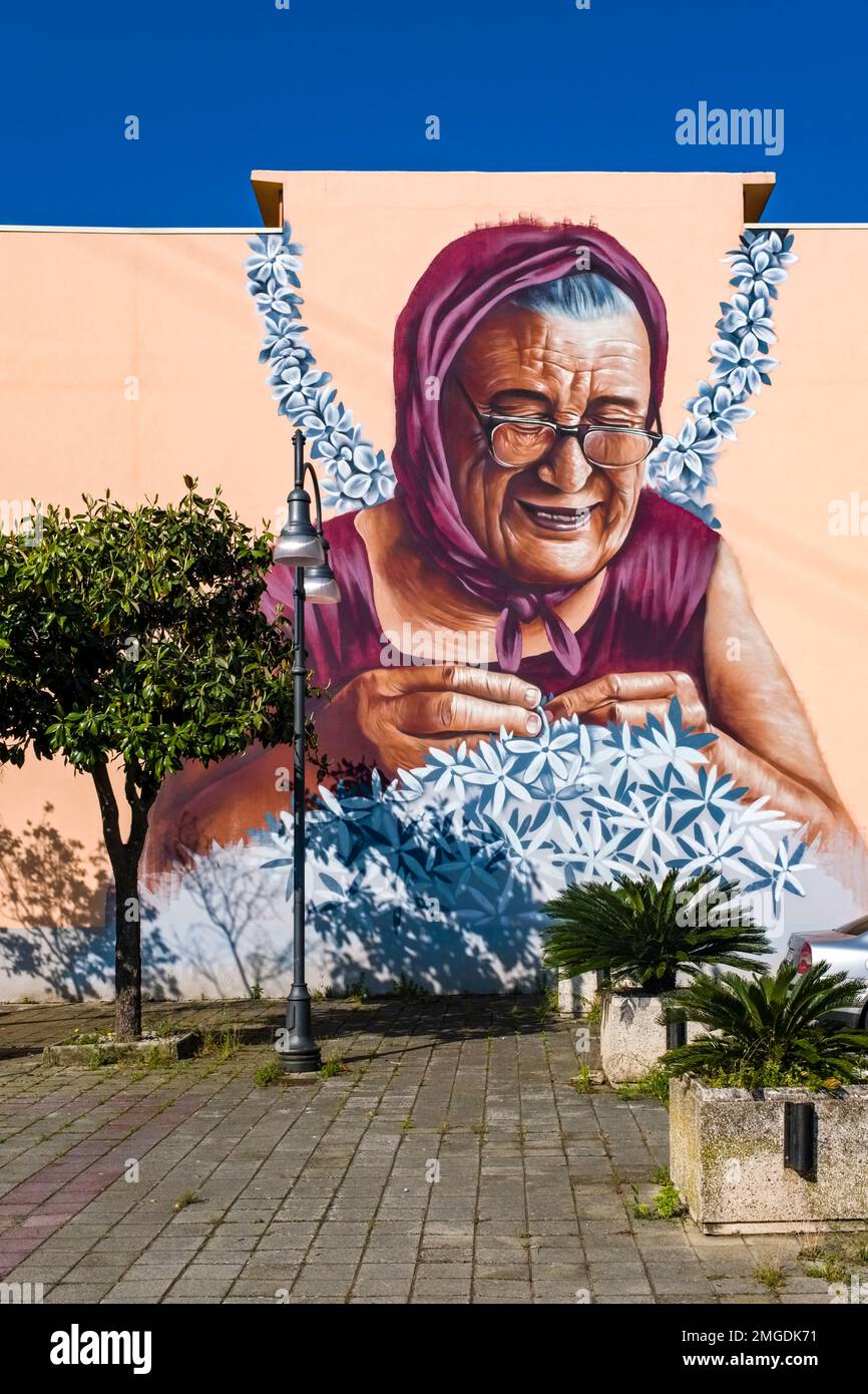 Große kunstvoll bemalte Graffität einer alten Dame, die Blumen an einer Hauswand in der Stadt Milazzo flechtete. Stockfoto