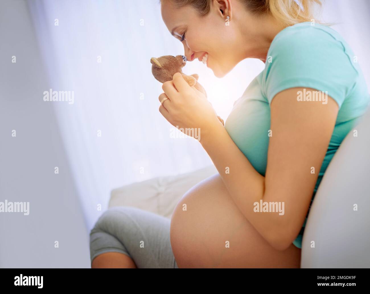 Ich kann es kaum erwarten, besondere Momente mit dir zu genießen. Eine schwangere Frau hält einen Teddybär, während sie sich zu Hause entspannt. Stockfoto