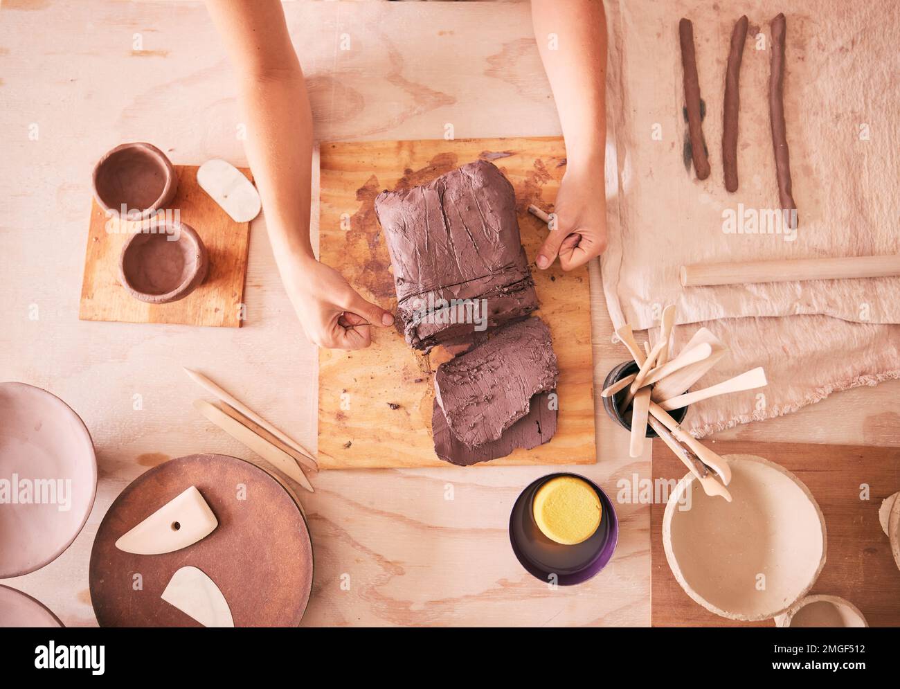 Töpferfrau und Hände mit Sicht von oben auf Ton am Tisch mit Werkzeugen für Produktion und Fertigung. Bildhauerprozess und handgefertigte Keramikwerkstatt von Stockfoto
