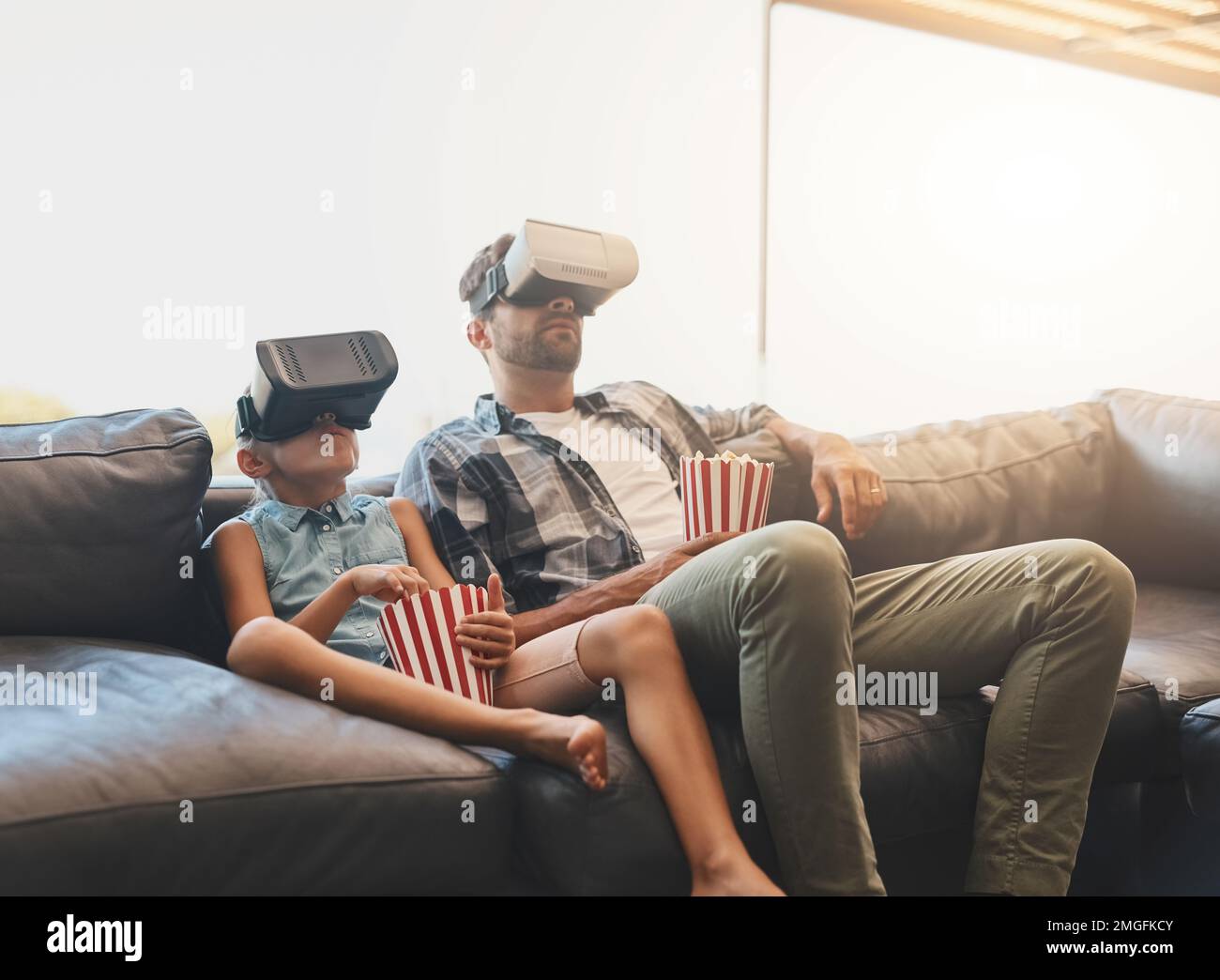 Simulation des Kinoerlebnisses. Ein Vater und eine Tochter essen Popcorn und sehen sich mit Virtual-Reality-Headsets zu Hause Filme an. Stockfoto