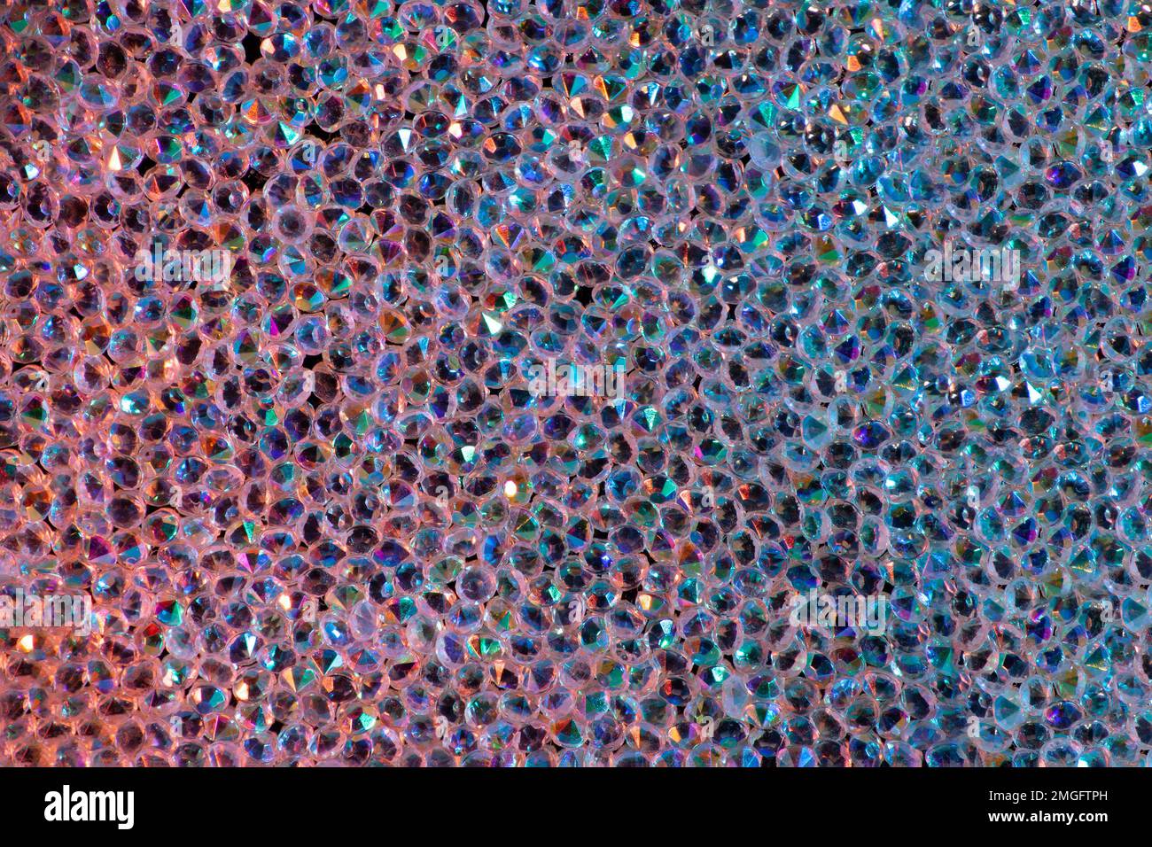 Abstrakter Strasssteinhintergrund. Textur von Strasssteinen, die mit mehrfarbigem Licht beleuchtet werden. Rosa und blaue glänzende Diamanten. Schließen. Leuchtfackeln auf Glas. Stockfoto