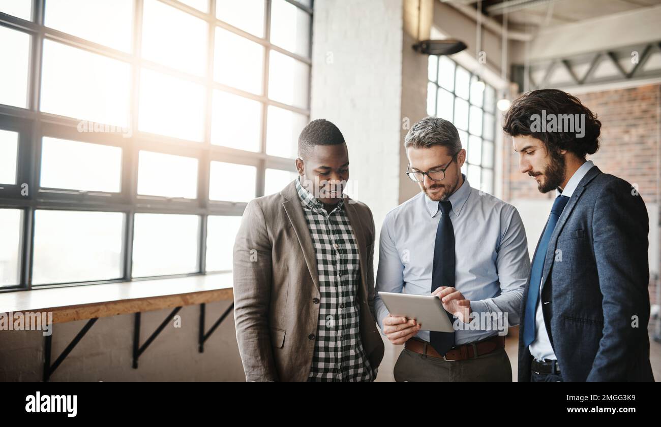 Drei Köpfe sind immer besser als einer. Drei gut gekleidete Geschäftsleute, die sich über ein Tablet in ihrem Büro ein Brainstorming aneignen. Stockfoto