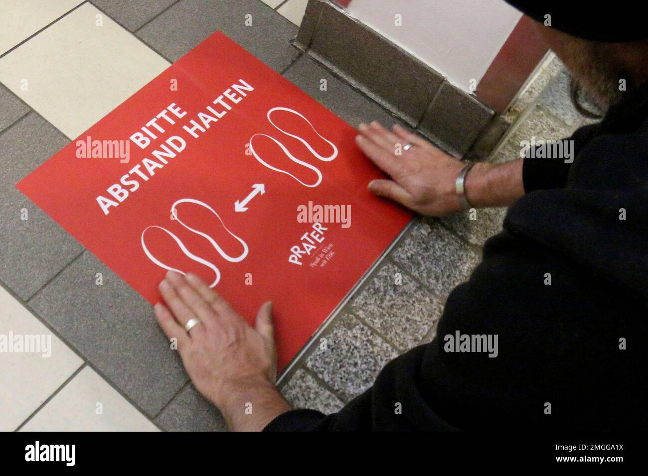 A worker places distance signs written on "Please keep your distance" the floor in a restaurant in Vienna, Austria, Thursday, May 14, 2020. In Austria restaurants may open again under certain conditions from Friday on. The Austrian government has moved to restrict freedom of movement for people, in an effort to slow the onset of the COVID-19 coronavirus. (AP Photo/Ronald Zak) Stockfoto