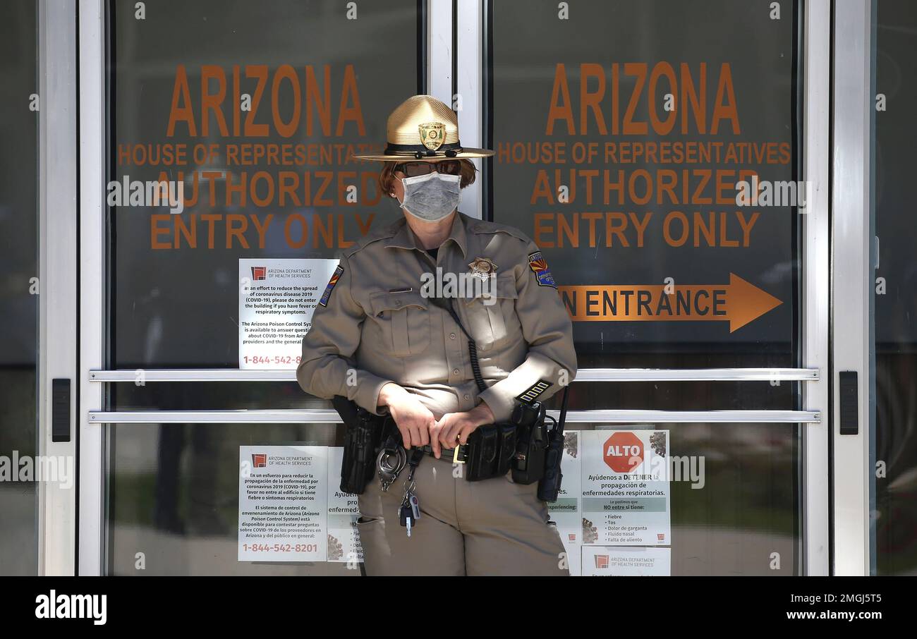 A Department of Public Safety police officer stands in front of the Arizona House of Representatives building as protesters rally at the state Capitol to 're-open' Arizona against the governor's stay-at-home order due to the coronavirus Monday, April 20, 2020, in Phoenix. (AP Photo/Ross D. Franklin) Stockfoto
