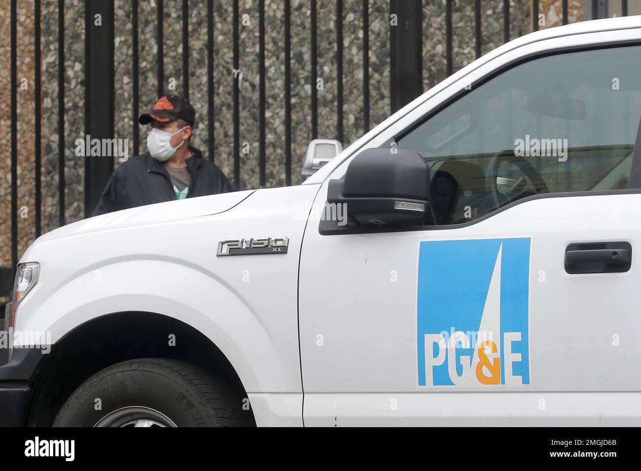 A man wearing a mask walks behind a Pacific Gas and Electric truck in San Francisco, Thursday, April 16, 2020. PG&E will face another legal challenge to a $13.5 billion settlement with more than 80,000 Northern California victims worried they're being shortchanged in a deal that's supposed to repay them for losses caused by the utility's negligence. (AP Photo/Jeff Chiu) Stockfoto