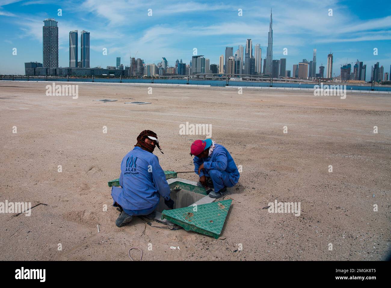 Two construction workers examine a drainage system with the Burj Khalifa, the world's tallest building, in the skyline behind them in Dubai, United Arab Emirates, Monday, April 6, 2020. Dubai, one of seven sheikdoms in the United Arab Emirates, is now under a 24-hour lockdown over the new coronavirus pandemic. (AP Photo/Jon Gambrell) Stockfoto