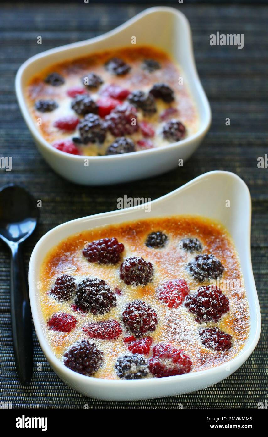 Obstgratin mit Beeren, Himbeeren, Brombeeren und Sahne in weißen Gerichten auf dem Tisch zum Dessert Stockfoto