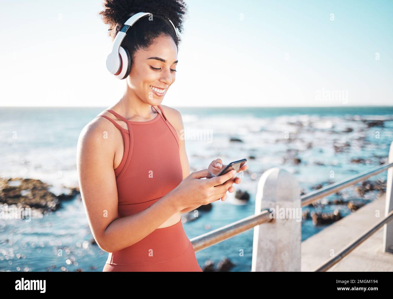 Schwarze Frau am Strand, Kopfhörer und Telefon mit Fitness, Läufer hört Musik für sportliche Motivation. Viel Spaß beim Online-Streaming mit Podcast oder Radio Stockfoto