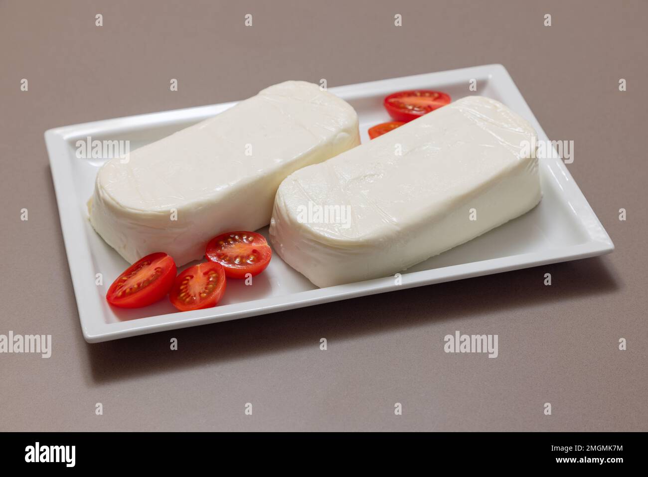 Stücke italienischen Kuhmozzarella für Pizza auf einem weißen rechteckigen Teller (selektiver Fokus) Stockfoto