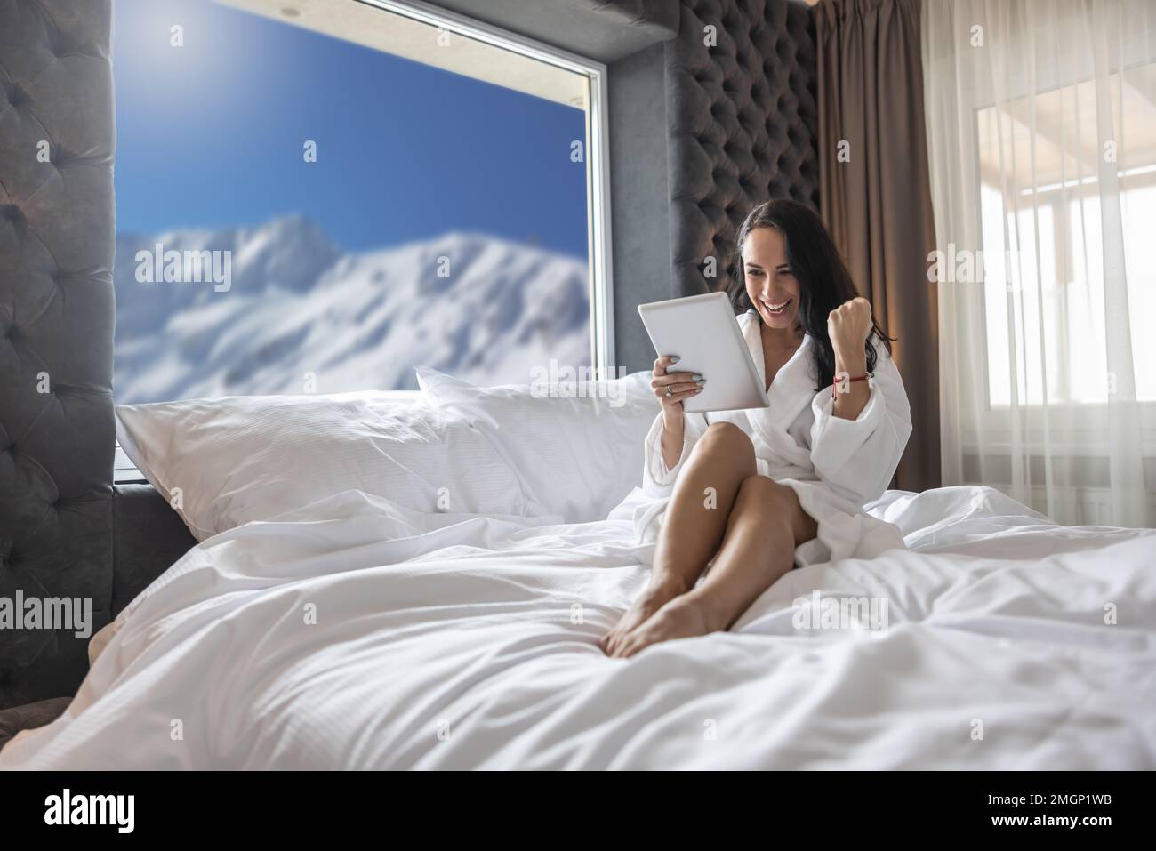 Junge Frau, die im Online-Lotto gewonnen hat, oder sie machte ein gutes Geschäft im Hotelzimmer mit einem fröhlichen Gesichtsausdruck. Stockfoto