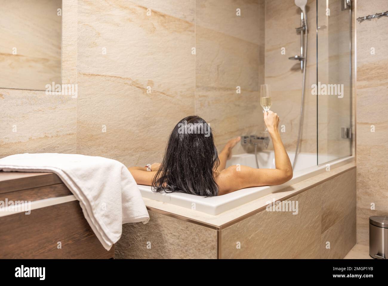 Eine wunderschöne Brünette genießt einen Abend allein in der Badewanne mit einem Glas Champagner. Stockfoto