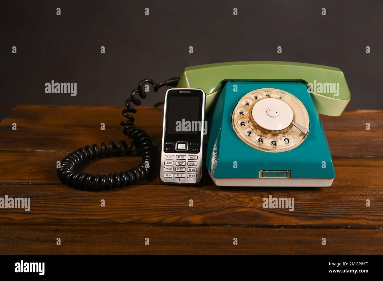 Ein altes altmodisches Telefon neben einem alten Mobiltelefon-Drucktastentelefon. Auf einem Holztisch. Stockfoto