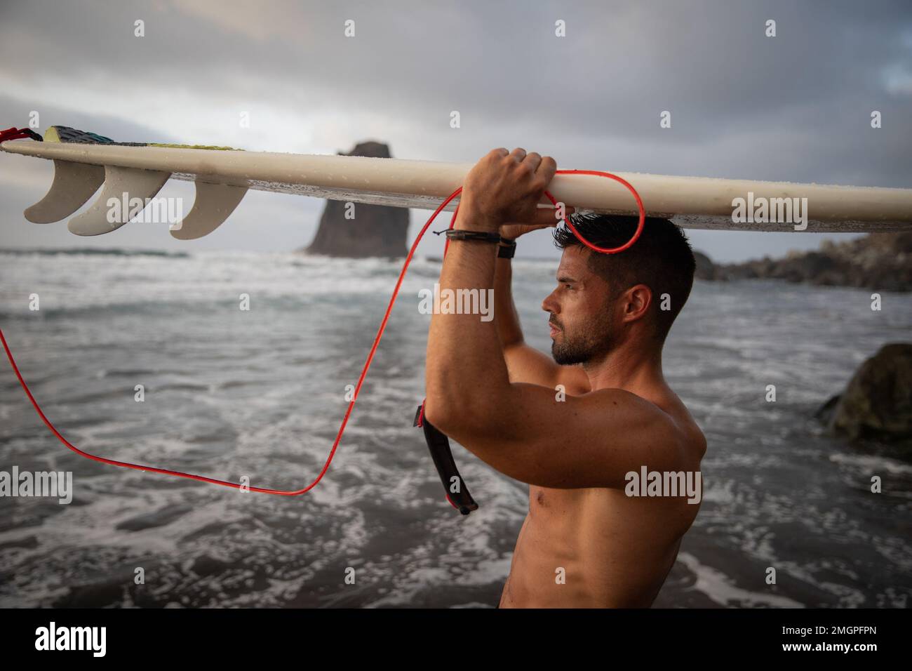 Ein Surfer legt sich sein Surfbrett auf den Kopf und schaut auf den Horizont Stockfoto