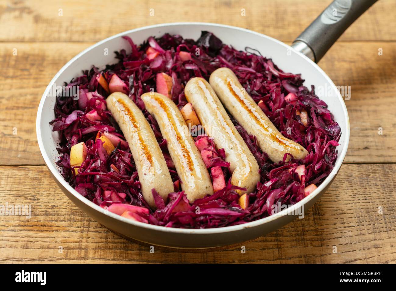 Bratpfanne mit geschmortem Rotkohl mit veganen Würsten und Apfelstücken. Stockfoto