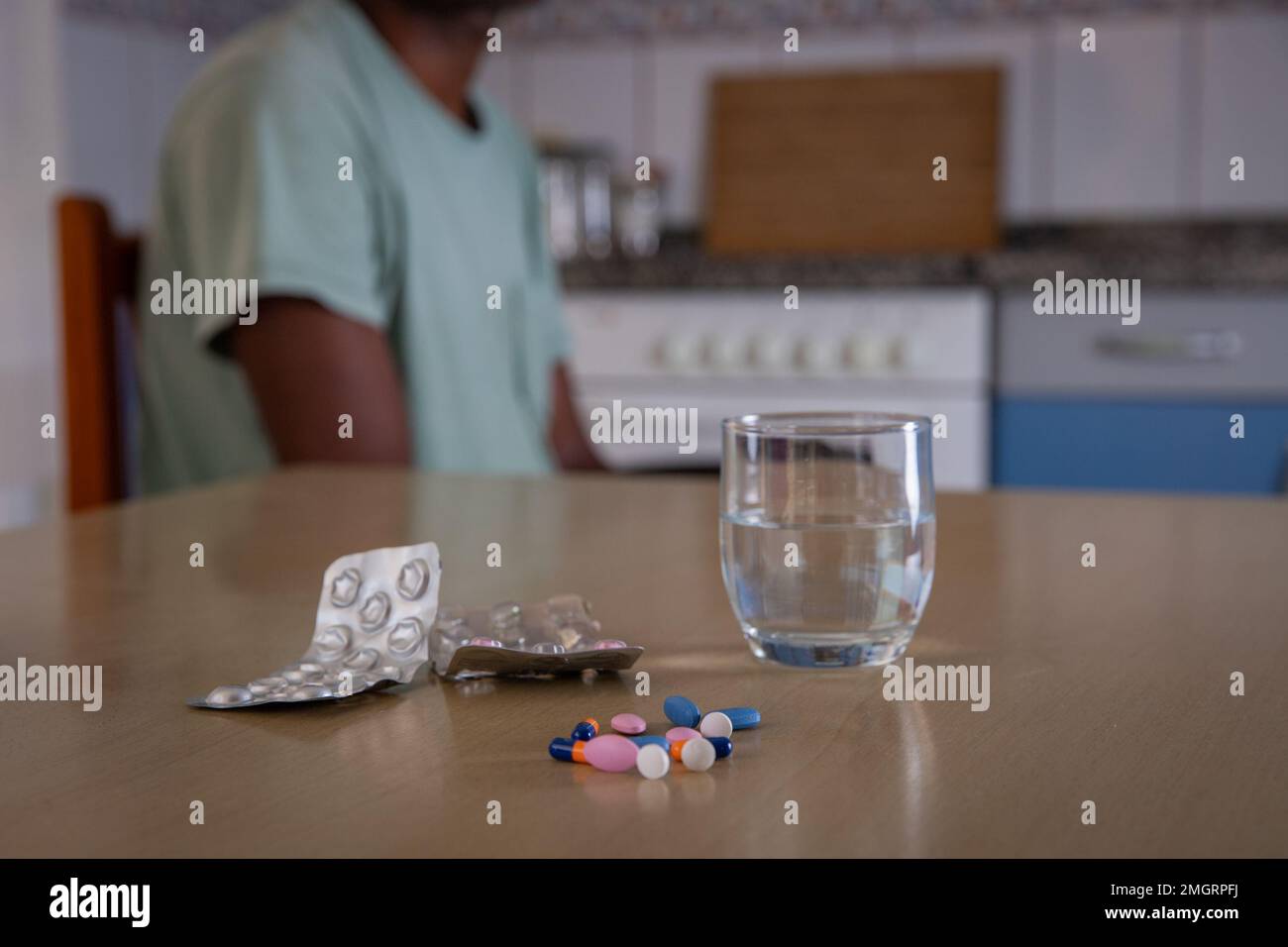 Nahaufnahme einiger Medikamente und ein Glas Wasser, Person, die dahinter sitzt, Konzept des Drogenkonsums Stockfoto