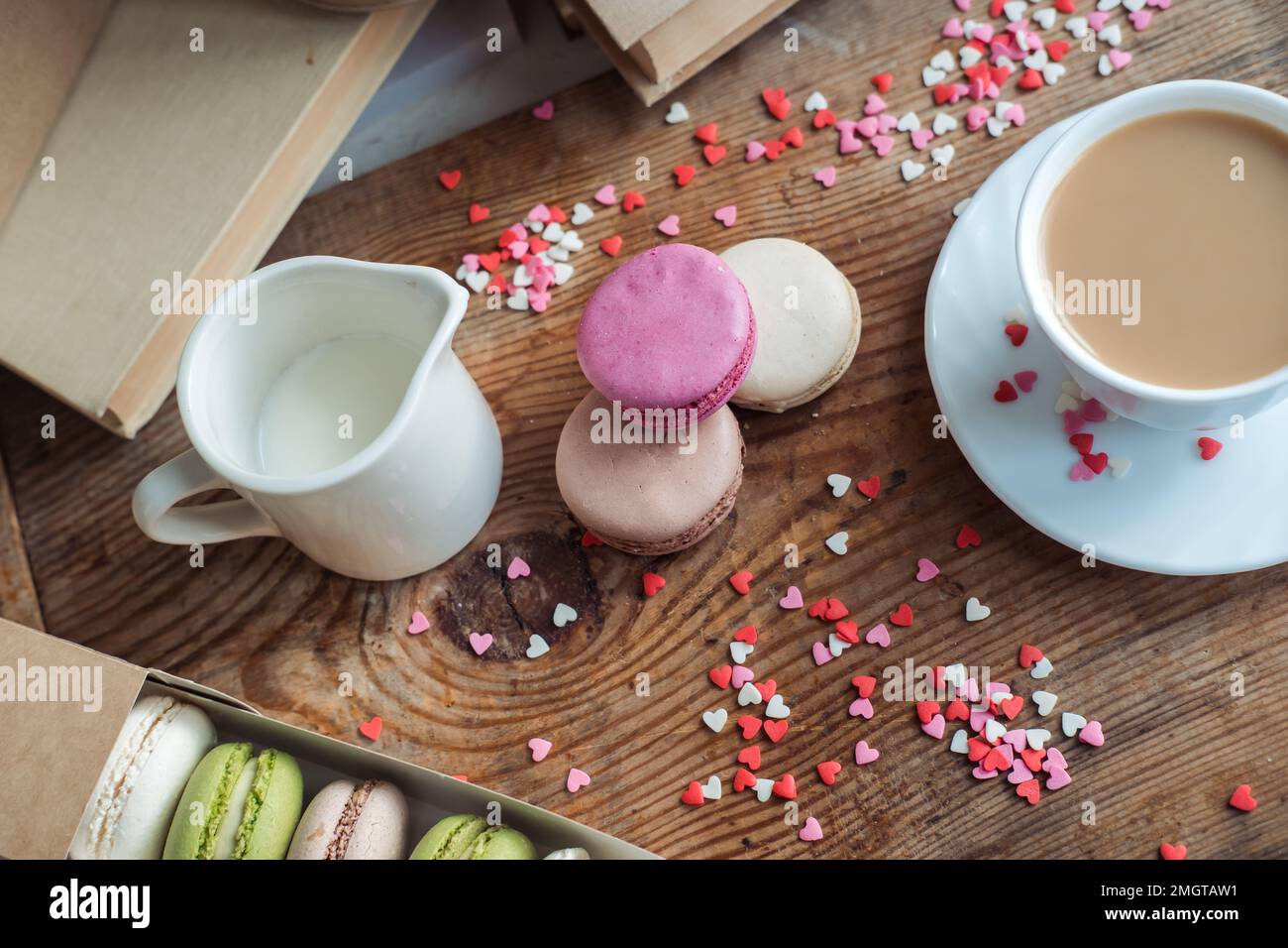 Makronen und eine Tasse Kaffee, ein Milchkännchen auf einem Hintergrund mit kleinen Herzen auf einem hölzernen Hintergrund, Draufsicht Stockfoto