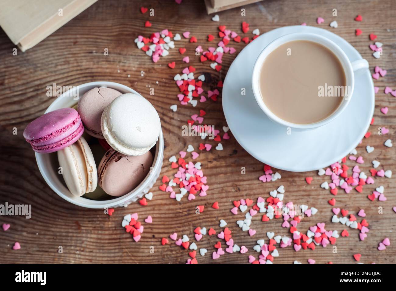 Makronen in einer Schüssel und eine Tasse Kaffee, vor dem Hintergrund kleiner Herzen auf einem hölzernen Hintergrund, Draufsicht Stockfoto