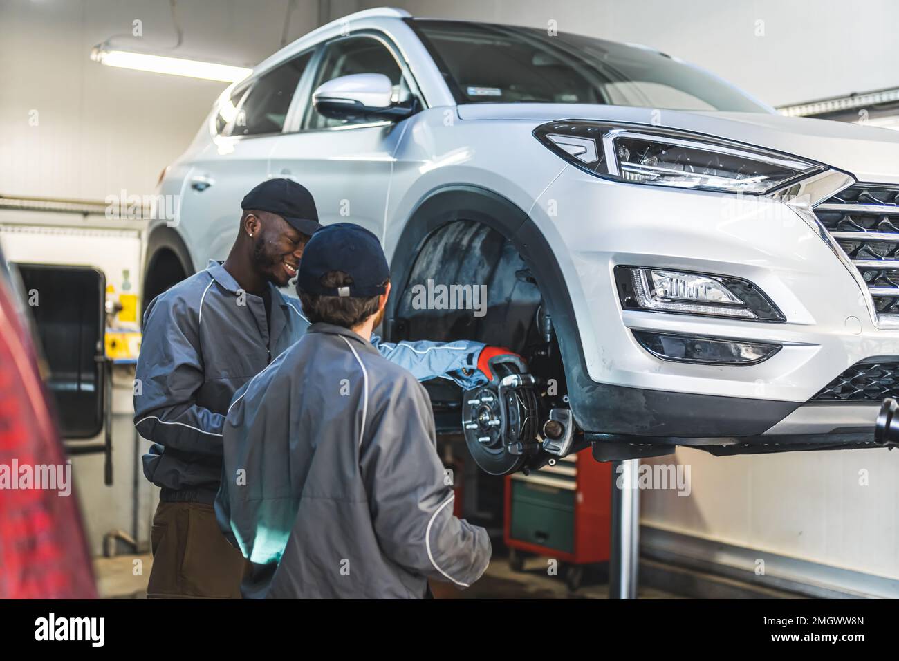 Zwei Mechaniker in der Nähe eines weißen Luxuswagens auf einer Hebebühne in einer Autowerkstatt, die Reifen repariert. Hochwertige Fotos Stockfoto