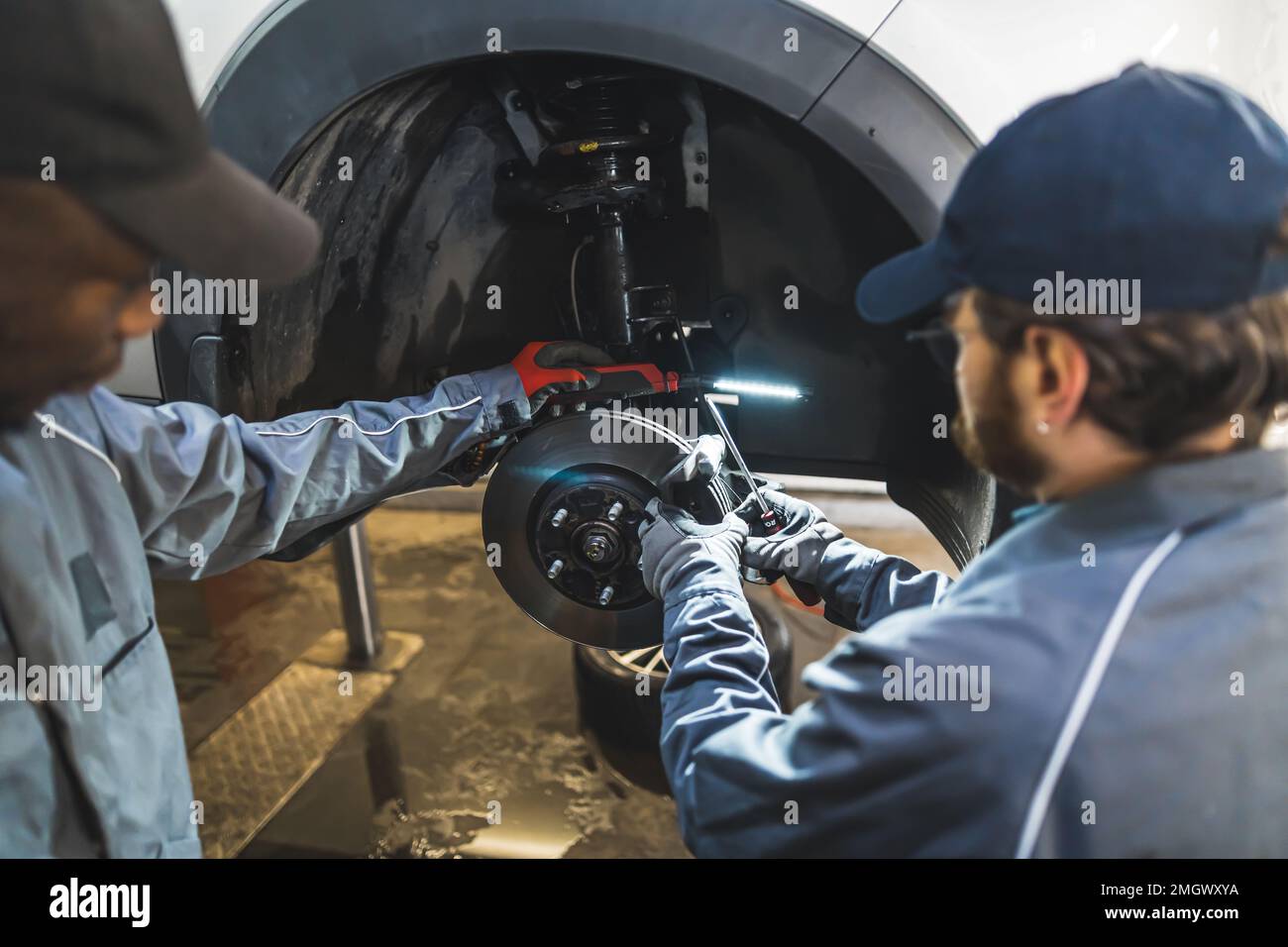 Mechaniker ersetzt Räder eines weißen Luxuswagens mit Werkzeugen in einer Autoreparaturwerkstatt. Hochwertige Fotos Stockfoto