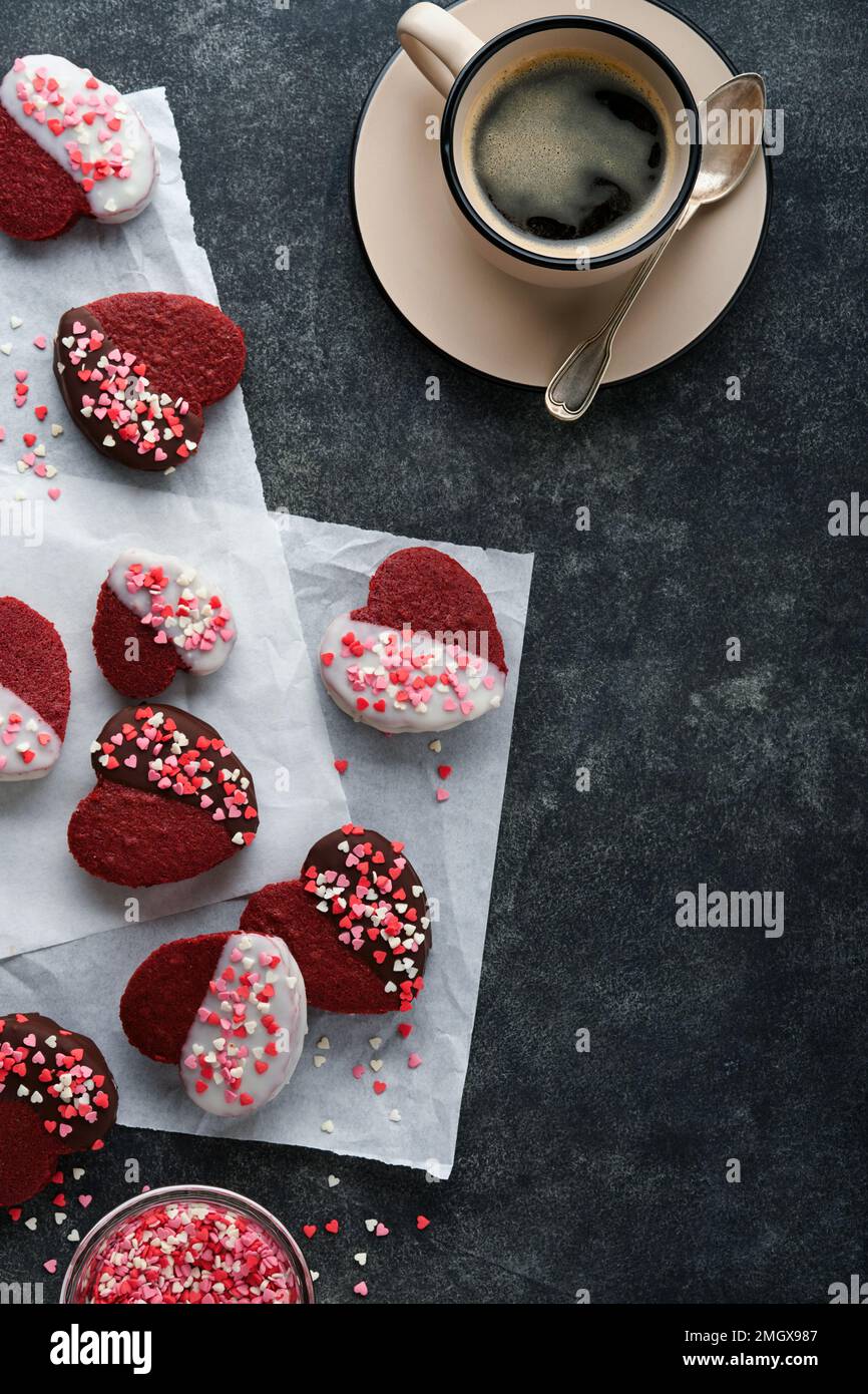 Rote Samt- oder Brownie-Kekse in Herzform in Schokoladeneis mit roten Rosen auf schwarzem Hintergrund. Dessert-Idee für Valentinstag, Mütter oder Frauen Stockfoto