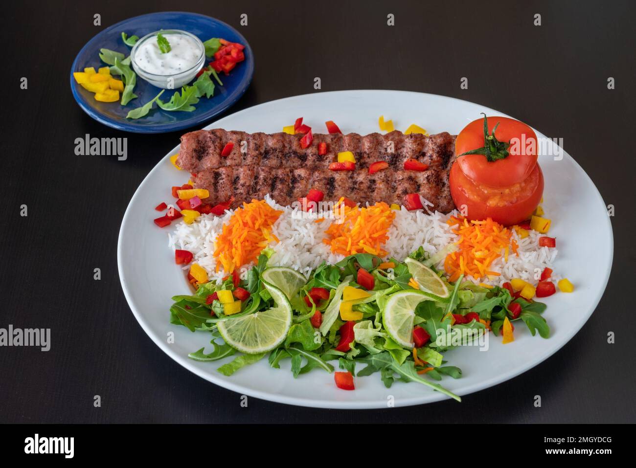 Lula Kebab vom Kalbfleisch mit Reis, Gemüse und Sauce auf schwarzem Hintergrund. Stockfoto