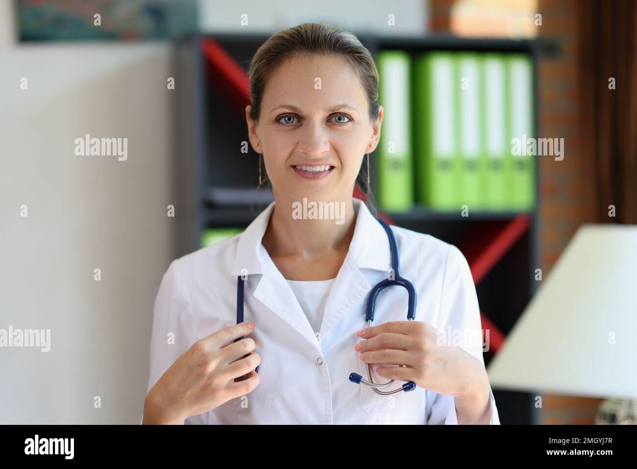 Glückliche Ärztin mit Stethoskop, die in der Arztpraxis auf die Kamera schaut. Stockfoto