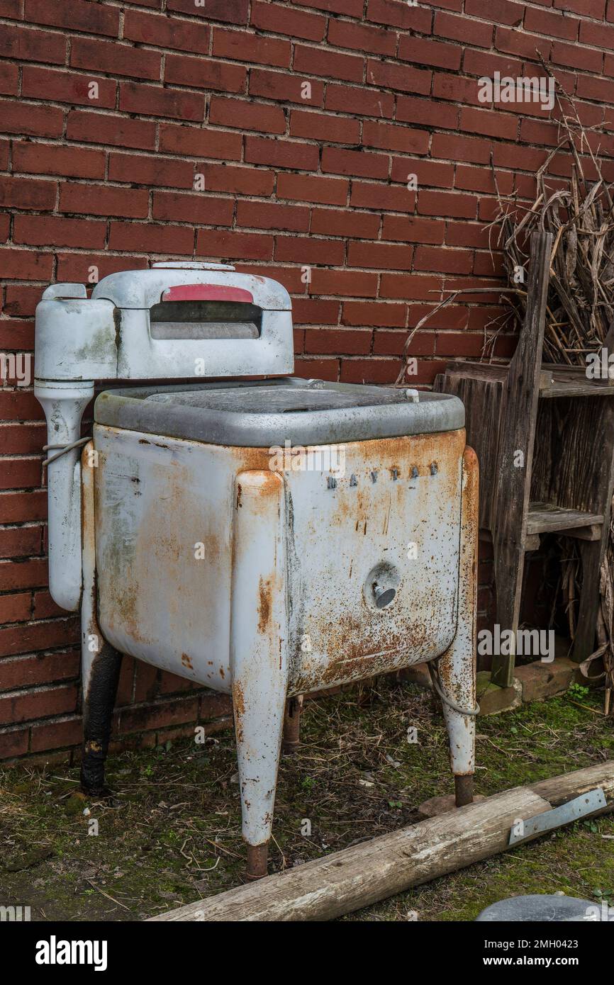 Eine alte, veraltete Maytag-Waschmaschine, die draußen an einem Gebäude rostet, komplett mit einem Motor Stockfoto