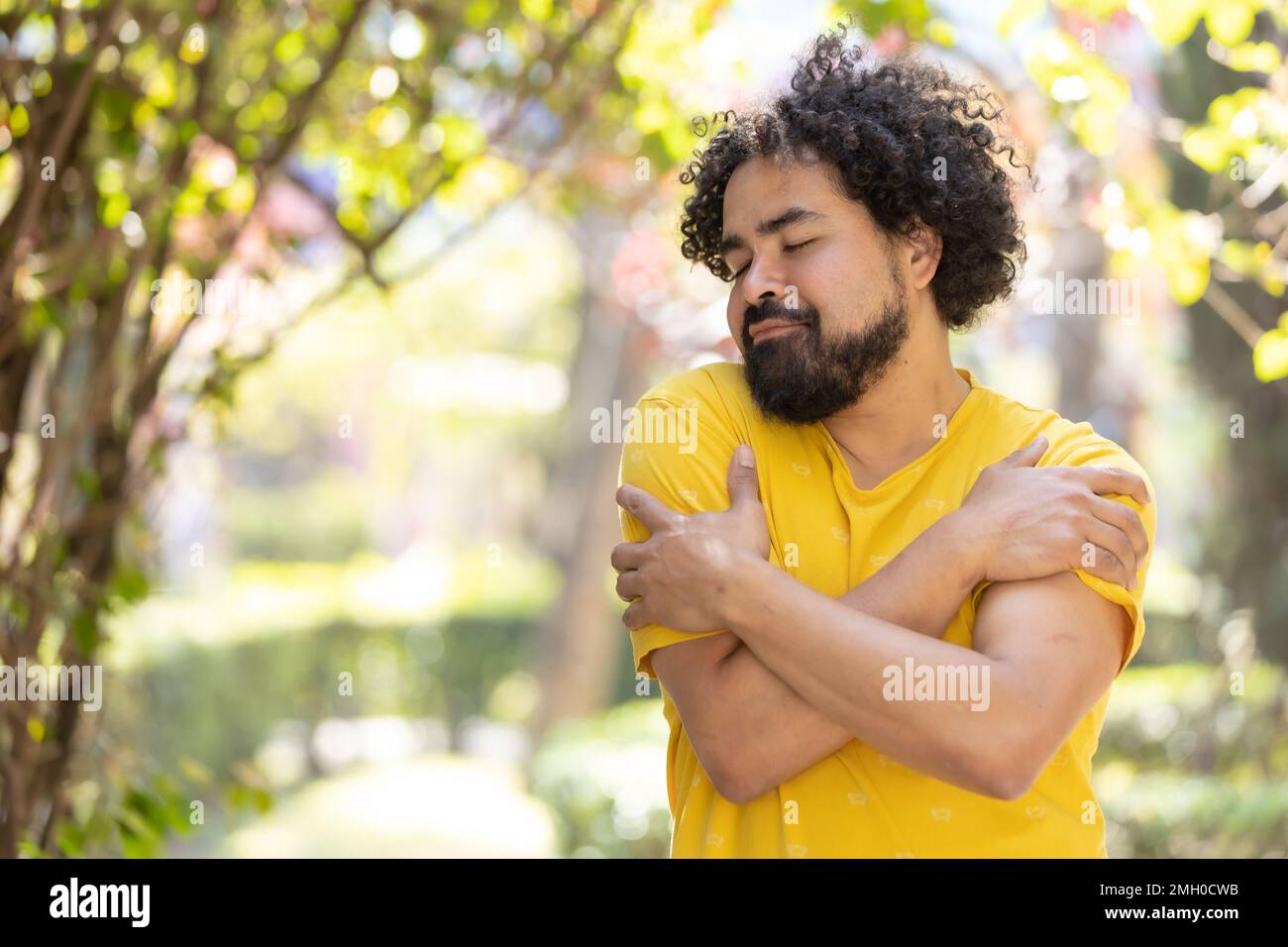 Junger Mexikaner mit Bart und Afro, der sich umarmt, Selbstliebe Stockfoto