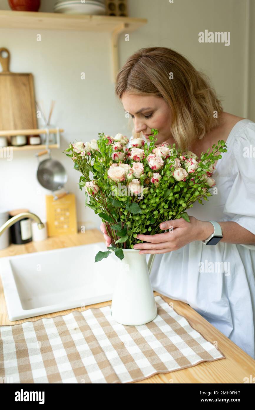 Eine Frau mittleren Alters steht in der Küche mit einem Blumenstrauß Stockfoto