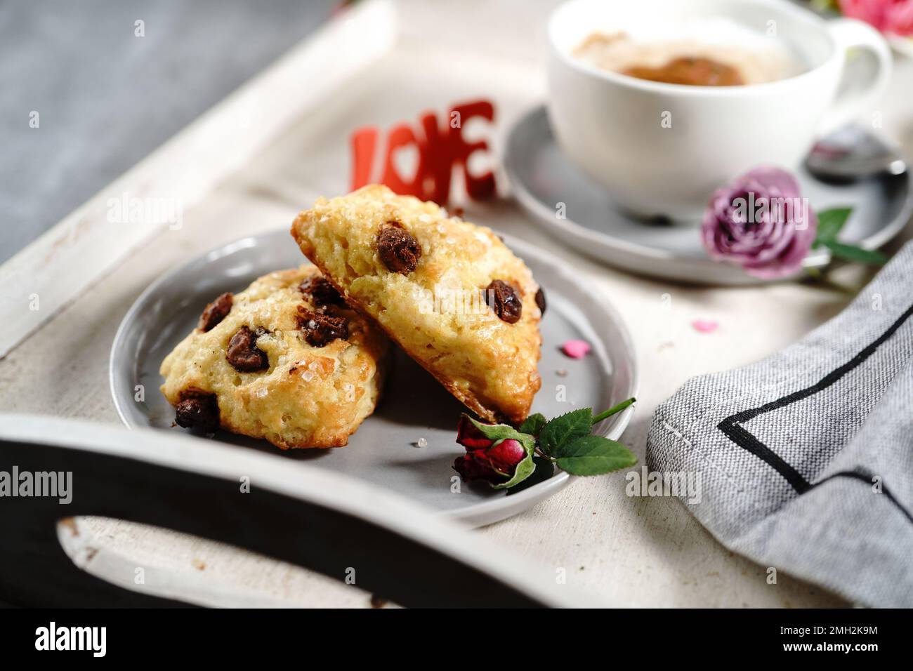 Frühstücksraum am Valentinstag - Scones Cappuccino Herz und Rosen auf einem Tablett, selektiver Fokus Stockfoto