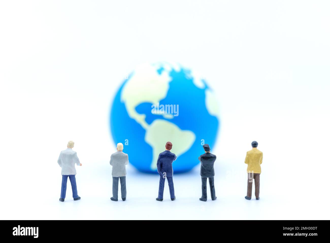 Konzept Der Globalen Geschäftsplanung. Nahaufnahme einer Gruppe von Miniaturfiguren, die auf weißem Hintergrund auf einen Mini-Weltball schauen. Stockfoto