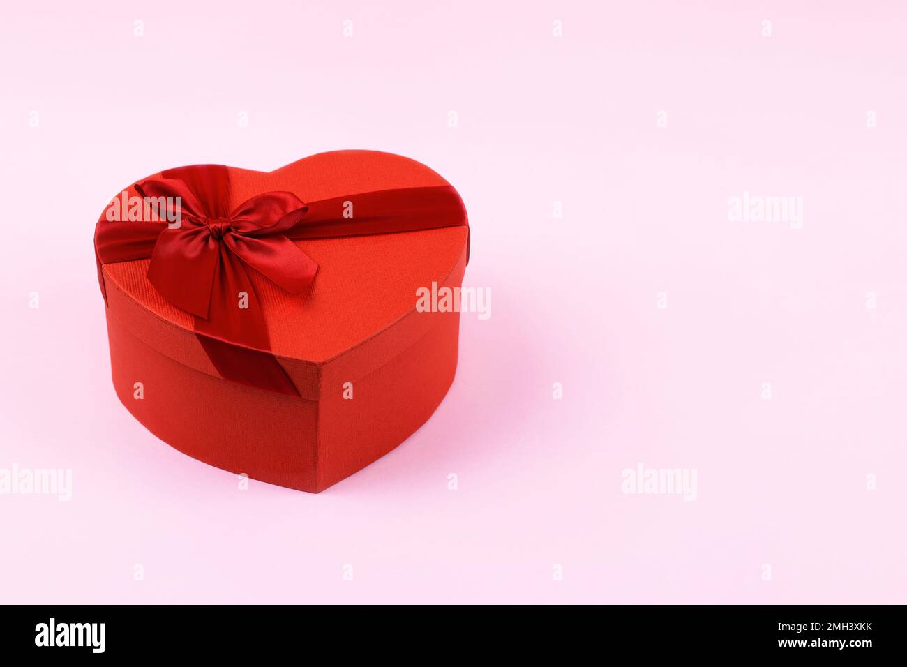 Rote Geschenkbox in Herzform mit roter Schleife auf pinkfarbenem Hintergrund und Platz für Text. Herzlichen Glückwunsch zum Valentinstag, Muttertag und Geburtstag Stockfoto