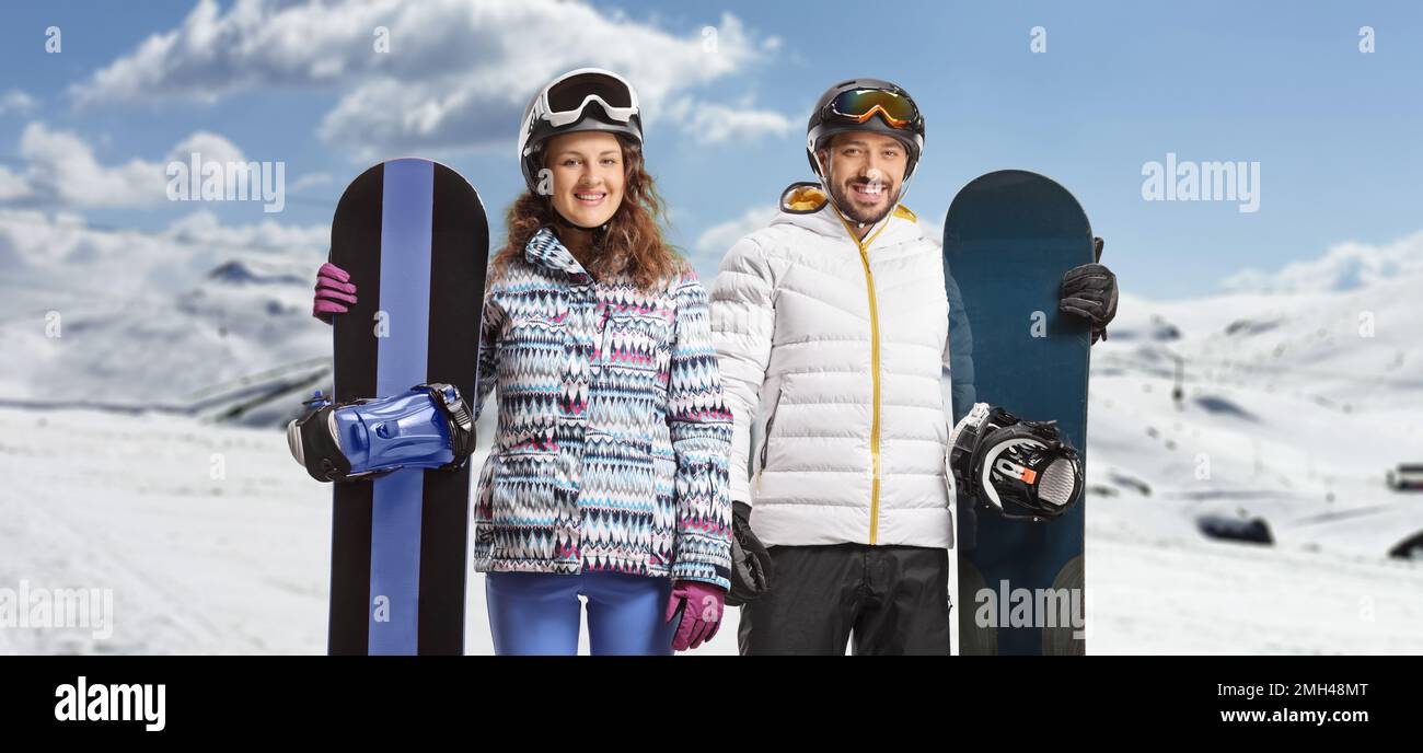 Junger Mann und Frau mit Snowboards, die auf einem verschneiten Berg posieren Stockfoto