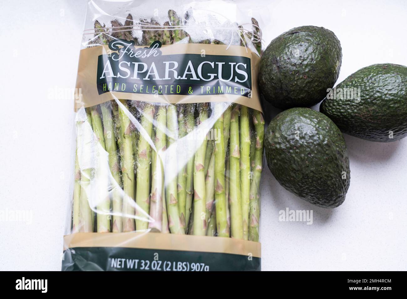 Frische Spargelspieße in einem Zellophan-Paket mit drei grünen unreifen Avocados daneben. Stockfoto