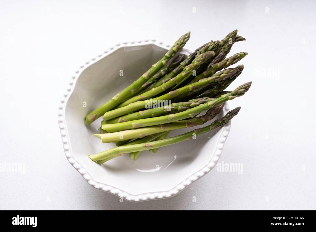 Frische rohe Spargelspitzen, Spargel officinalis, in einer weißen Schüssel auf weißem Hintergrund. Stockfoto