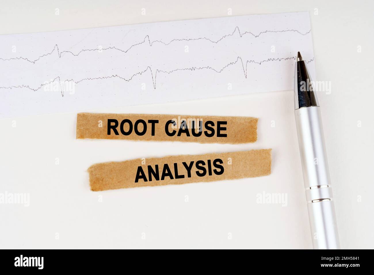 Medizinisches Konzept. Auf dem EKG liegt ein Stift und zerrissenes Papier mit dem Text – Ursachenanalyse Stockfoto