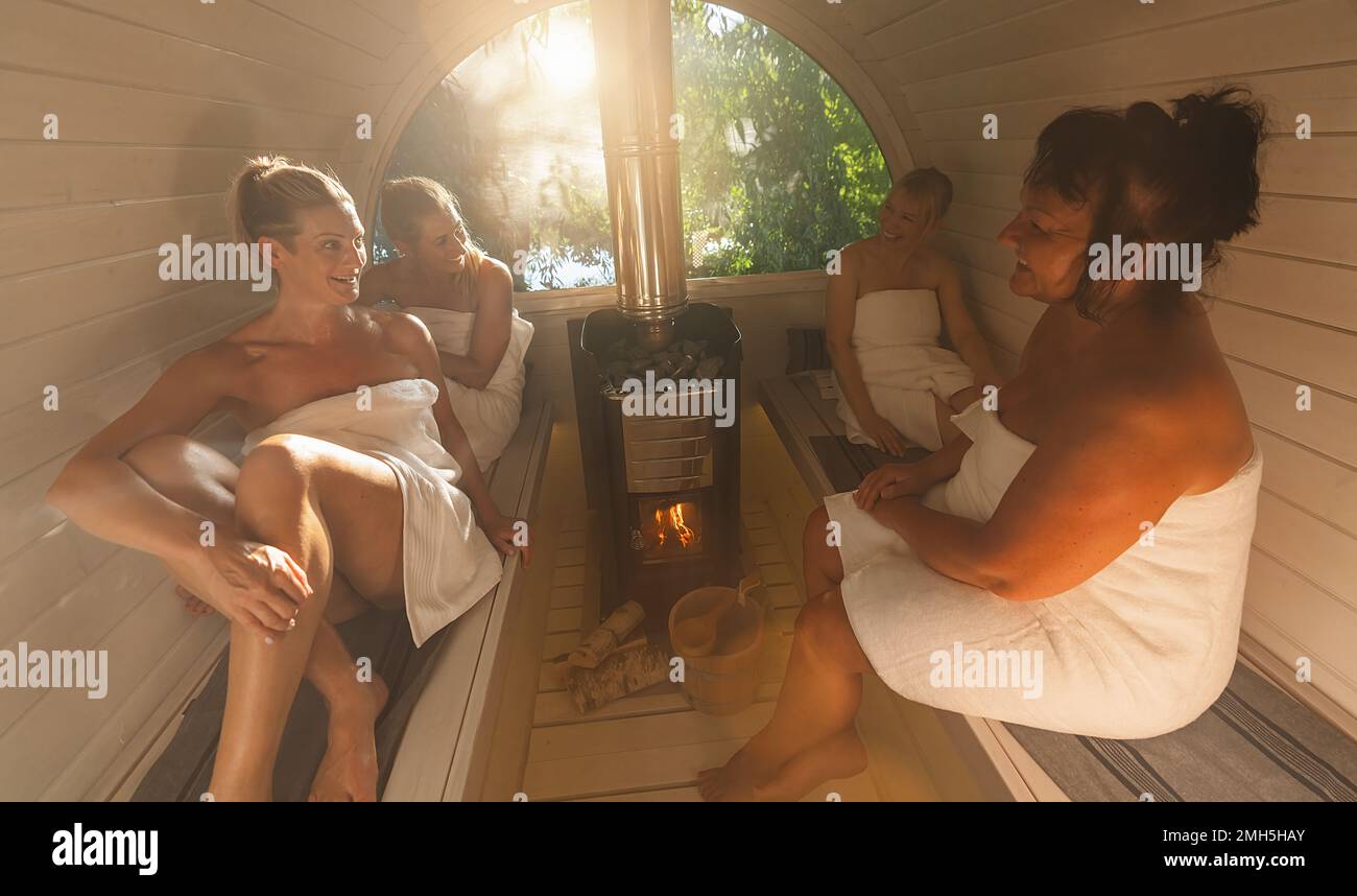 Glückliche Freundinnen, die sich in der hölzernen Fass-Sauna in norwegen entspannen. Die Leute entspannen sich und genießen den Urlaub, während sie sich in der finnischen Saunakabine entspannen. Stockfoto