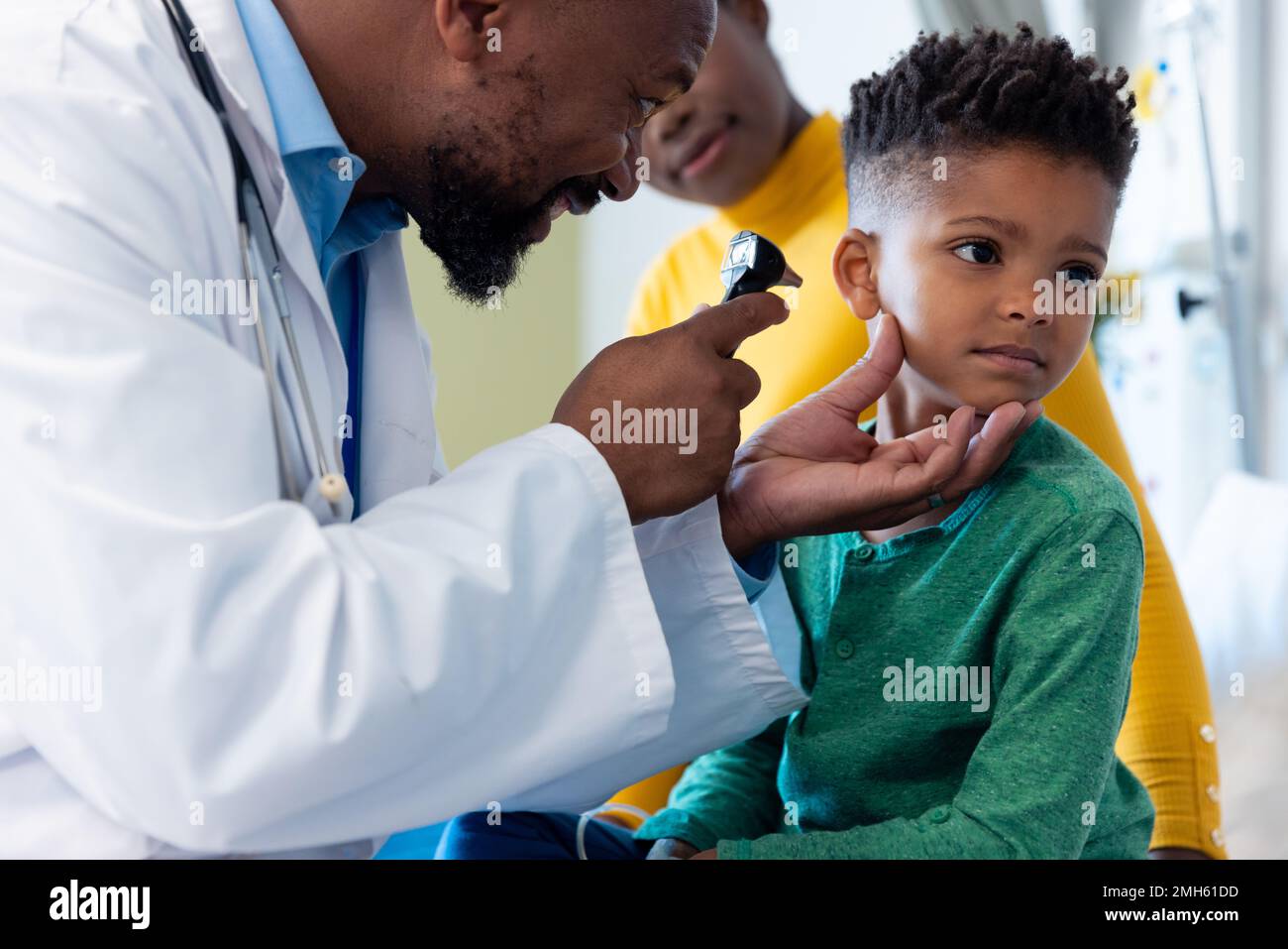 afroamerikanischer Arzt mit Otoskop zur Untersuchung des Gehörs eines Jungen mit Mutter Stockfoto