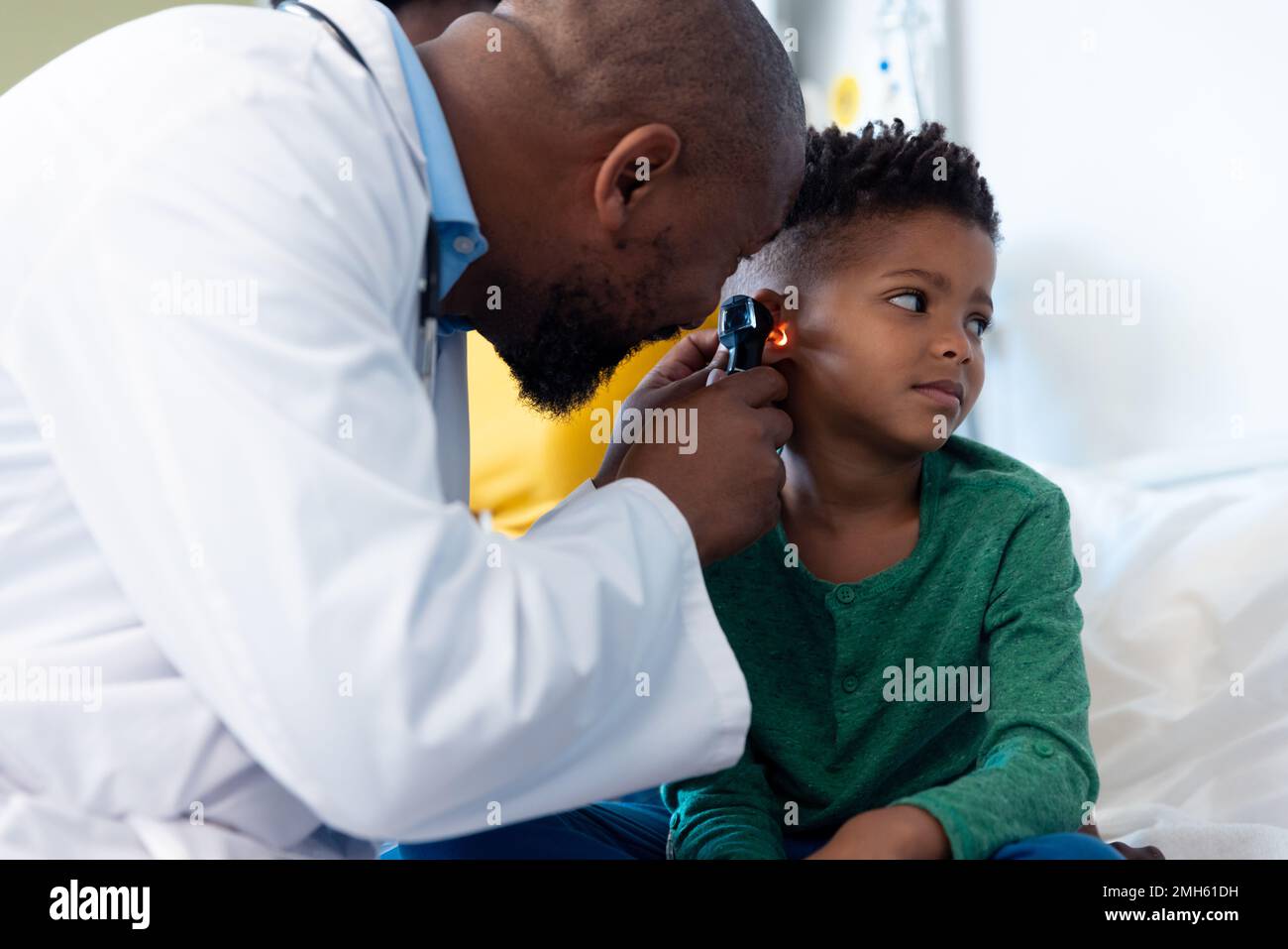 afroamerikanischer männlicher Arzt mit Otoskop zur Untersuchung des Gehörs eines Jungen im Krankenhaus Stockfoto