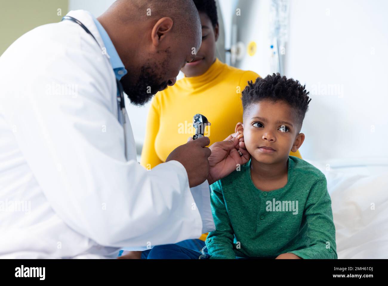afroamerikanischer Arzt mit Otoskop zur Untersuchung des Gehörs eines Jungen mit Mutter Stockfoto
