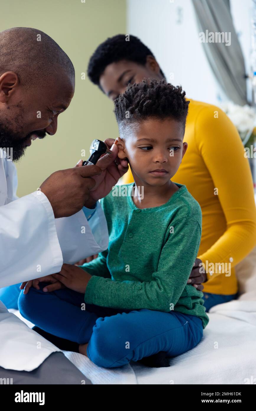 afroamerikanischer männlicher Arzt mit Otoskop zur Untersuchung des Ohrs eines Jungen mit Mutter Stockfoto