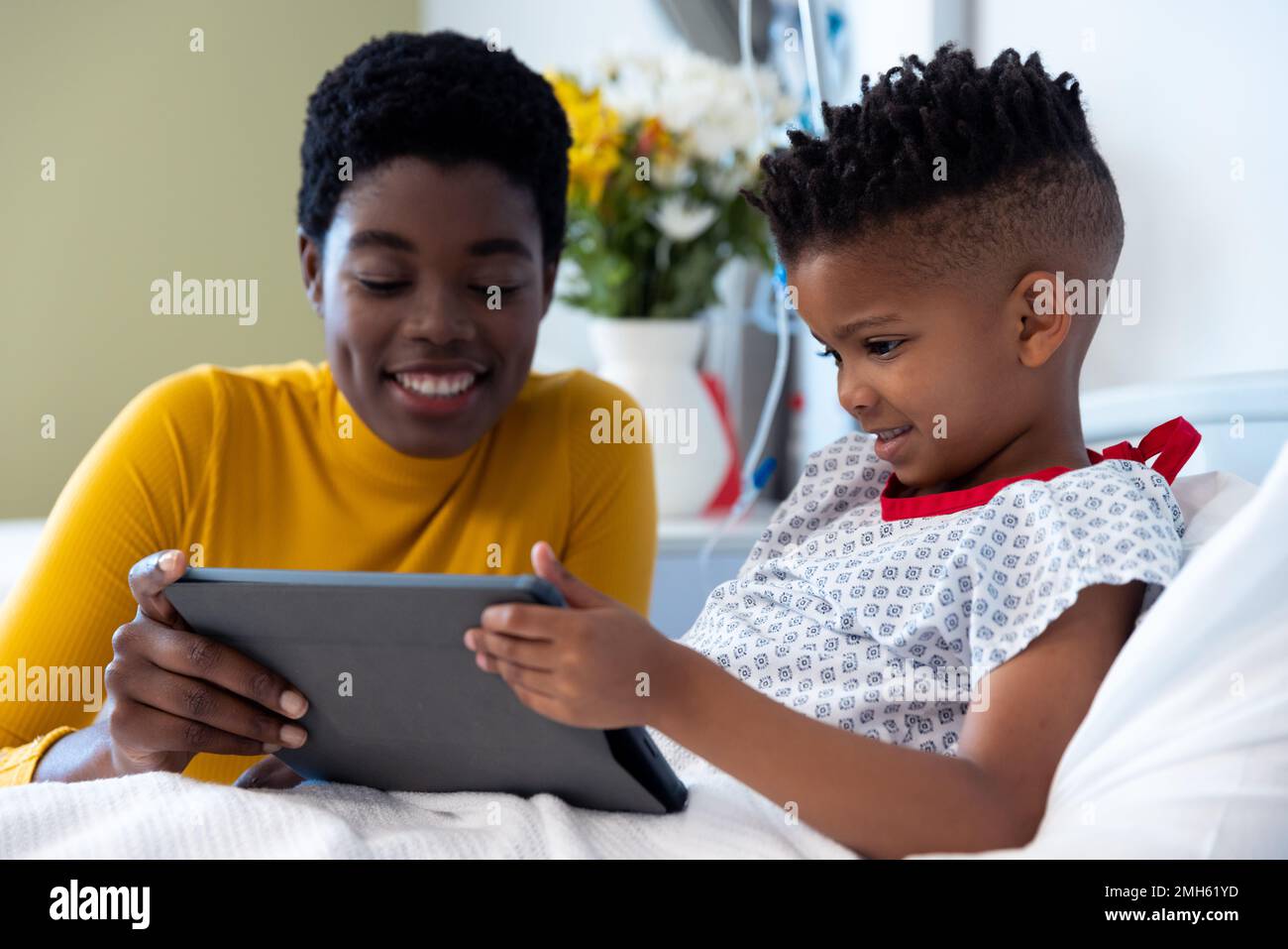 Glückliche afroamerikanische Mutter und Sohn Patient im Krankenhausbett, mit Tablet Stockfoto
